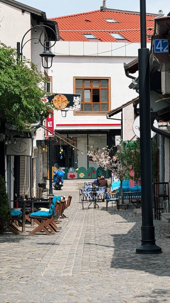 Cobbled street in Prizren lined with outdoor seating and a pizza restaurant sign