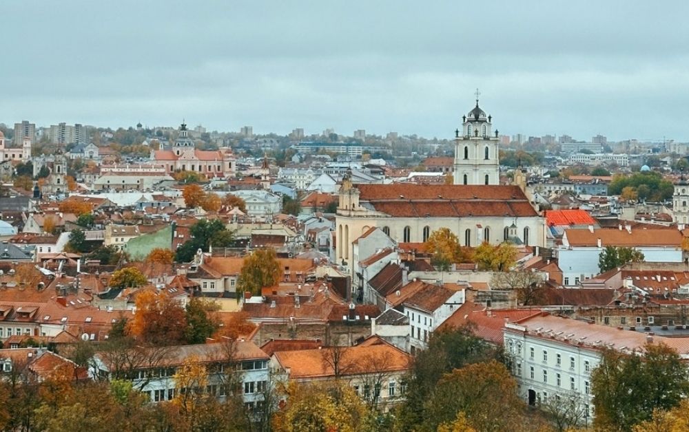 Panoramic view of Vilnius featuring red-tiled rooftops and a large white church tower under a cloudy sky