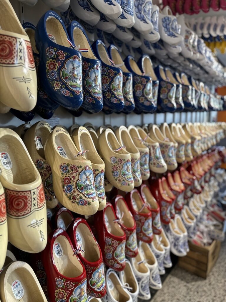 Rows of traditional wooden clogs painted blue, red, and natural wood with floral and windmill designs hanging on a shop wall