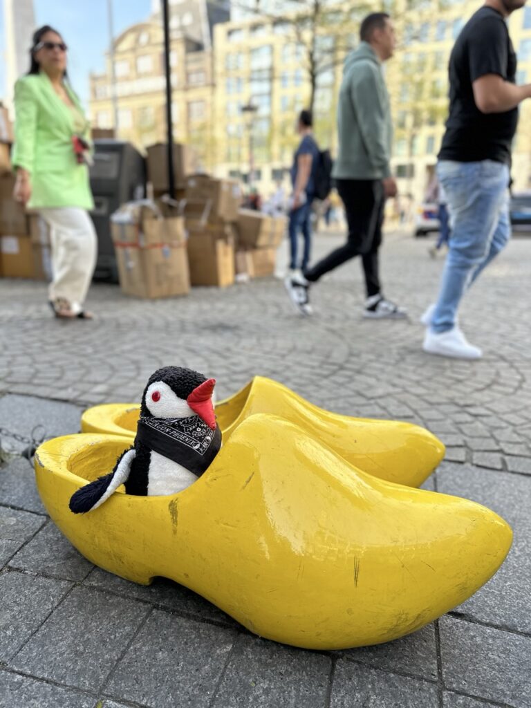 Miško the knitted penguin sits inside a giant yellow wooden clog on a cobblestone street in the Netherlands