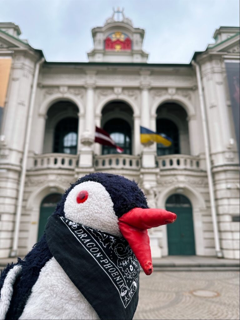 A plush penguin toy standing beside a sign