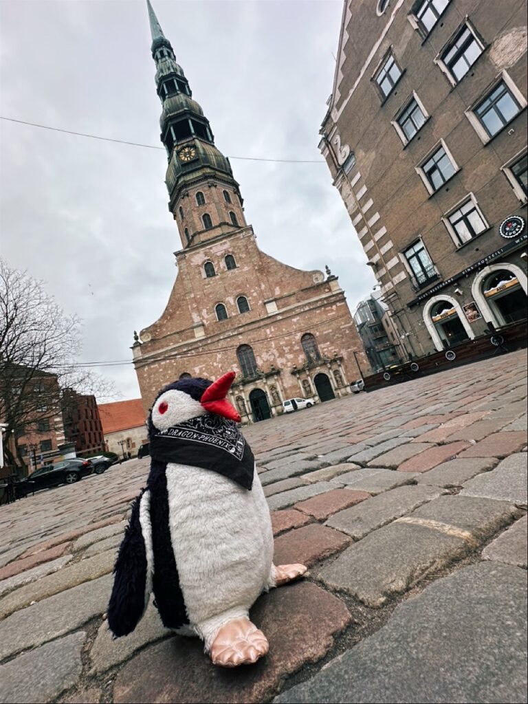 A woolen penguin toy with a beak perched beside a sign