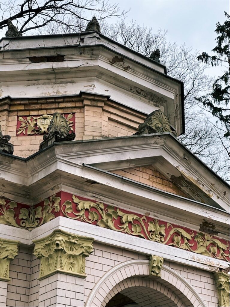 Low angle view of a building corner in Riga with red and gold floral friezes, green capitals, and a date plaque near the roof
