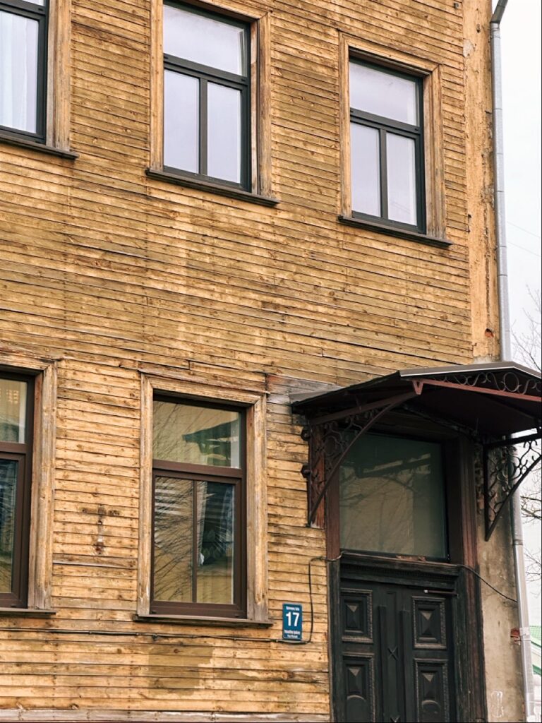 Wooden building facade in Riga with dark windows and a door under a metal awning next to house number 17