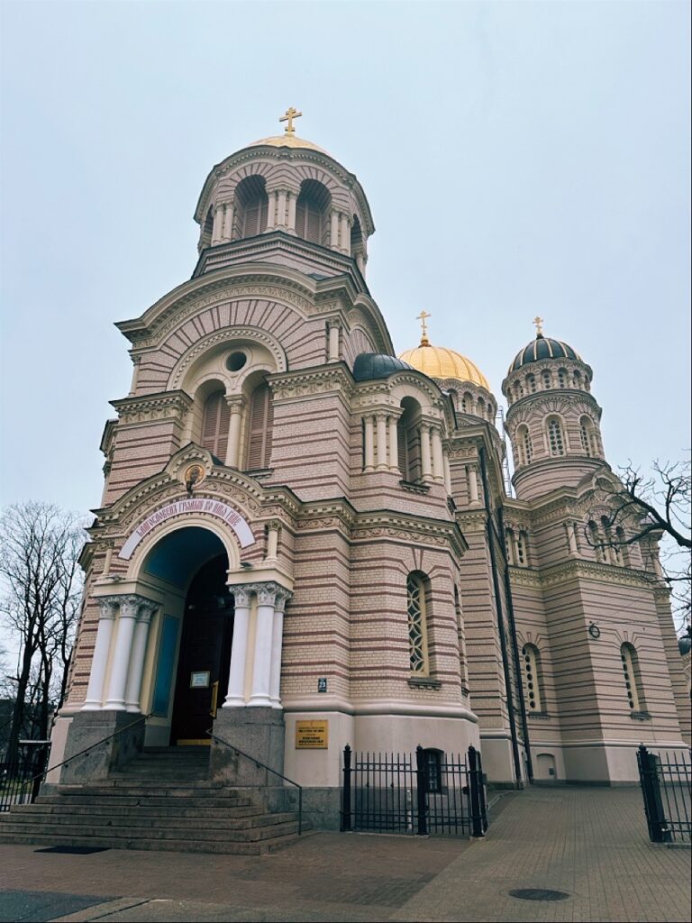 A low angle view of a pink and white striped cathedral with golden domes in Riga