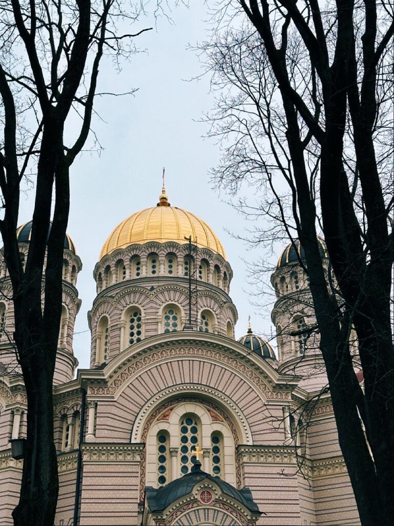 A cathedral with a large golden dome and striped brick walls framed by bare trees in Riga