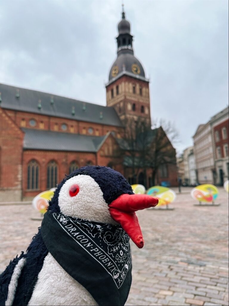 A plush penguin toy perched beside the Key To Riga sign