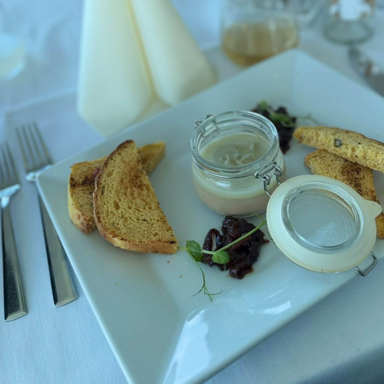 A white square plate with a small glass jar of pâté, toasted bread slices, and a dark garnish served at VEŽA Bratislava
