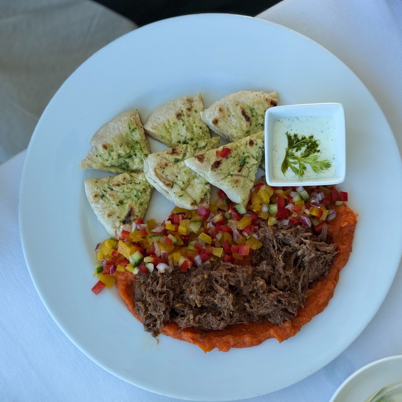 A plate with shredded meat colorful vegetables flatbread pieces and a small bowl of sauce at VEŽA Bratislava