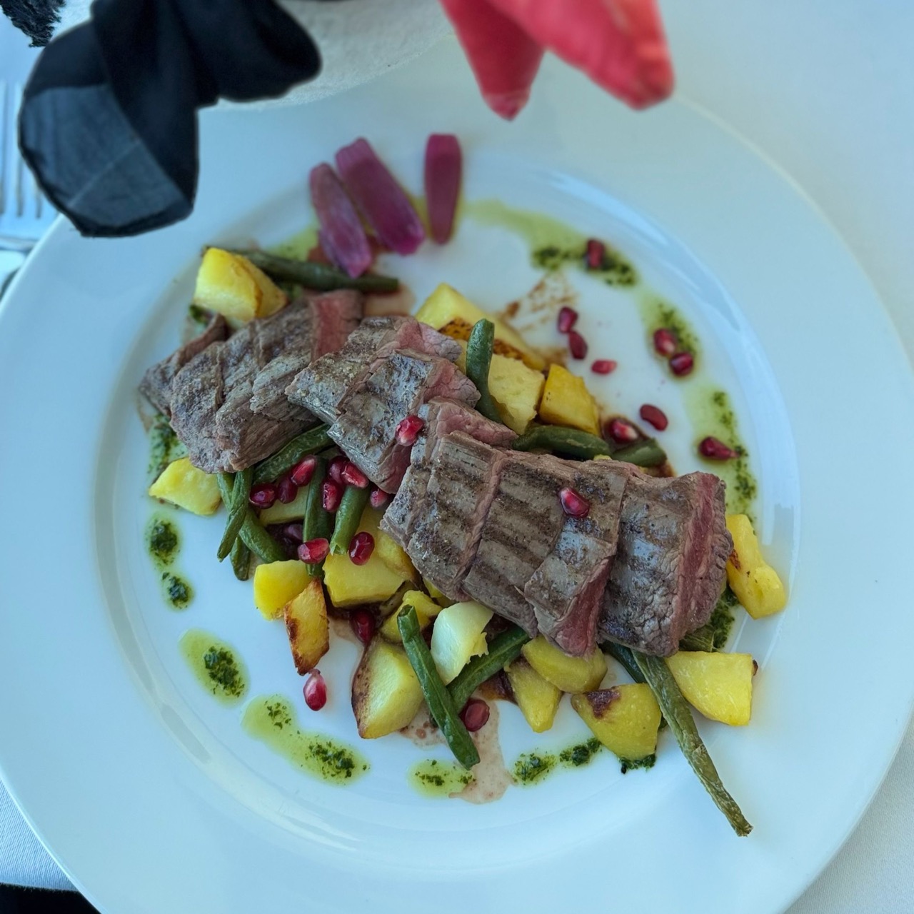 Sliced steak with roasted potatoes, green beans and pomegranate seeds on a white plate at VEŽA Bratislava while Miško looks on