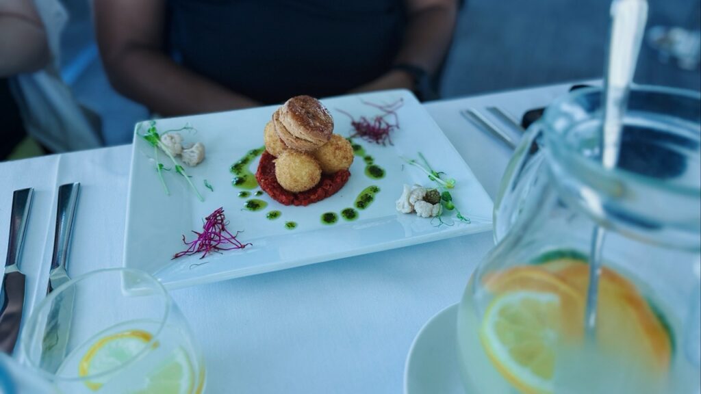 Stacked fried balls on red sauce with green oil garnish on a white plate next to a pitcher of lemonade at VEŽA Bratislava