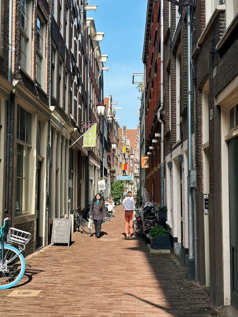 Narrow brick street in Amsterdam flanked by tall buildings with people walking and bicycles parked along the sides