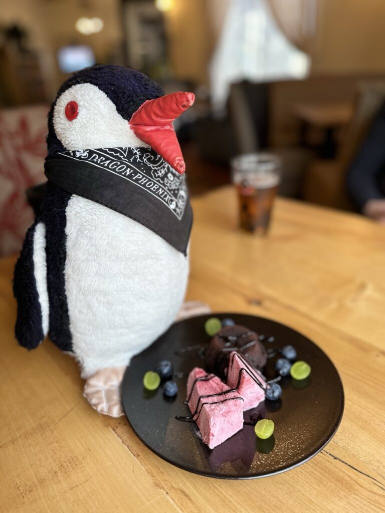 A plush penguin toy perched on a decorated cake beside a sign