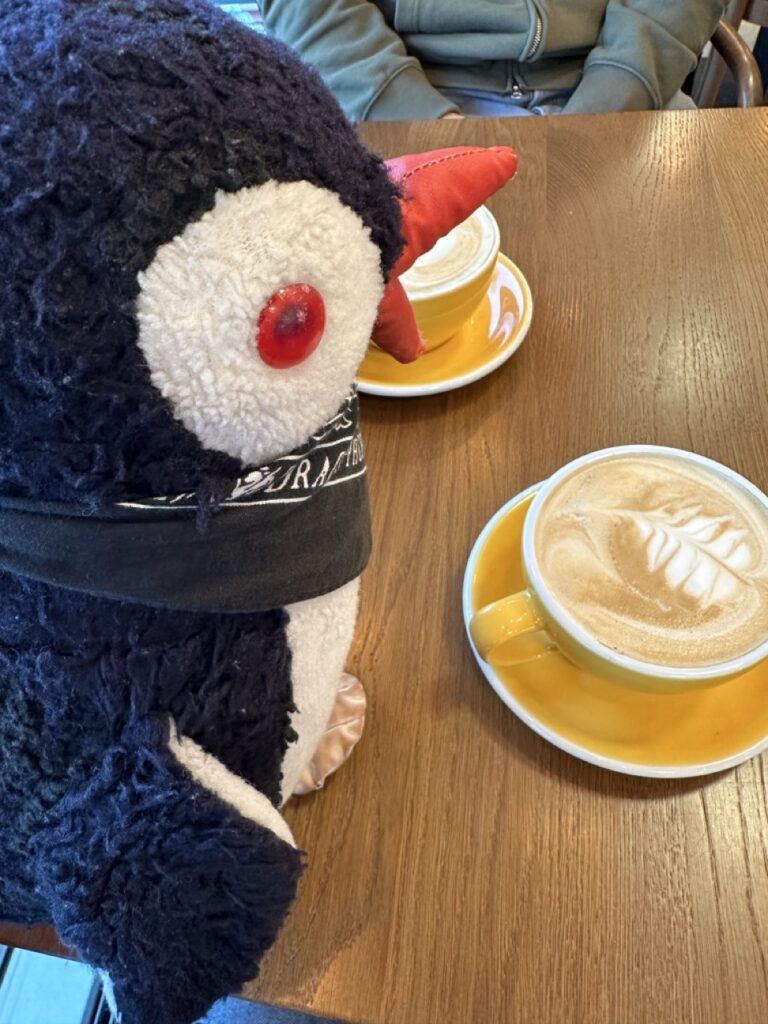 Stuffed penguin plush perched on a cup beside a sign