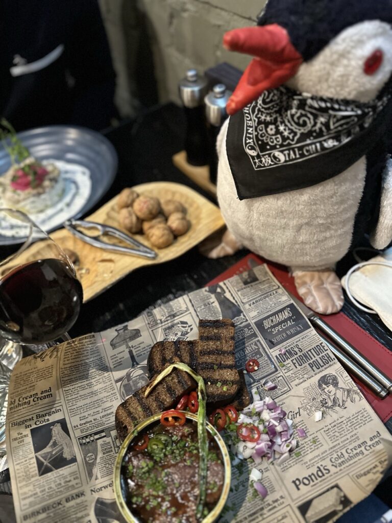 A plate of food beside a plush penguin toy on a table, with a sign in the background