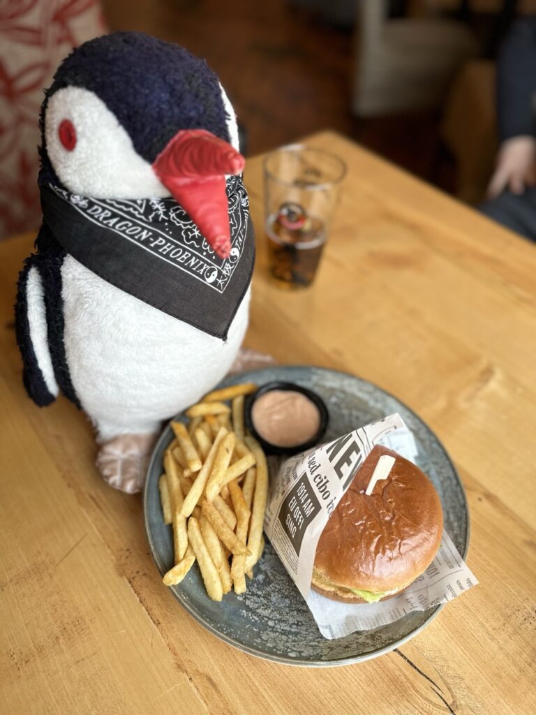 Stuffed penguin toy perched beside a plate of food with a sign in the background