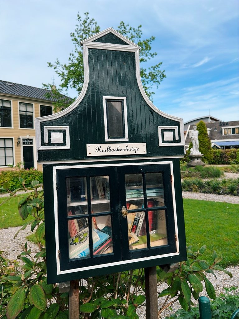 Dark green wooden miniature house in Zaanse Schans labeled Ruilboekenhuisje is a book exchange with books visible behind glass doors