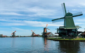 Four traditional windmills stand along the water at Zaanse Schans under a blue sky with wispy clouds