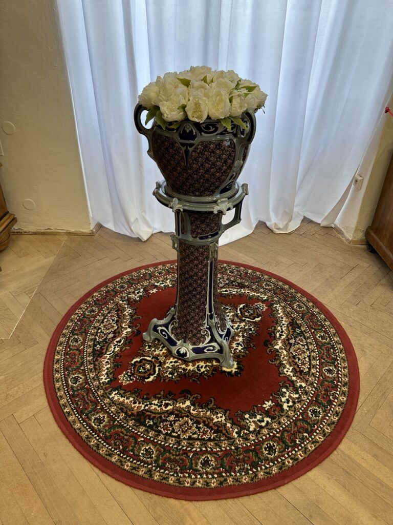 White flowers sit in an ornate pedestal vase on a round rug
