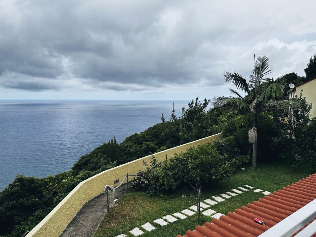 Tiled roof, lawn, and walkway overlooking a lush green hillside and ocean in Madeira