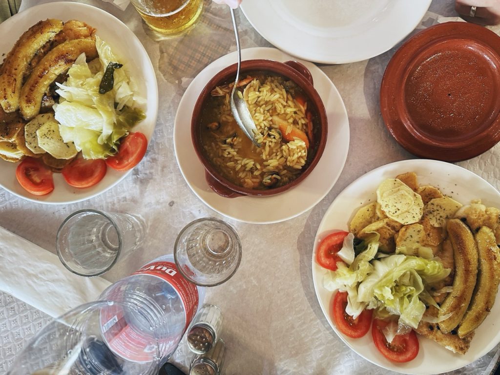 Overhead view of plates with seafood rice, fried bananas, and salad in Madeira