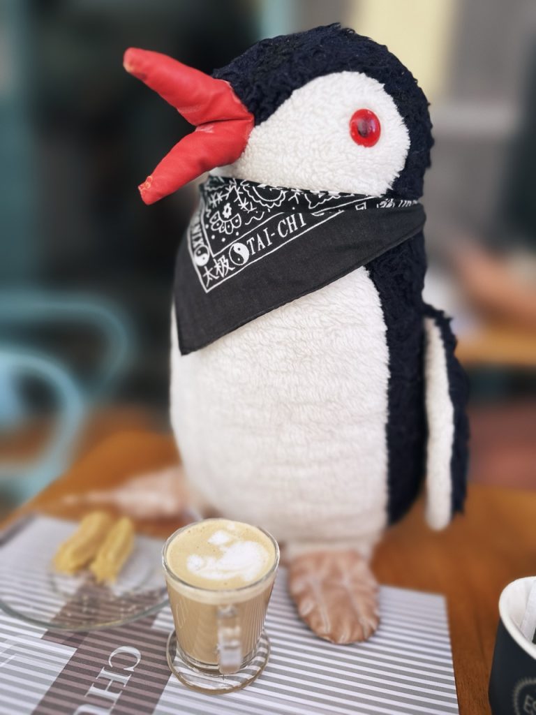 Plush penguin wearing a bandana sits next to a coffee and churros
