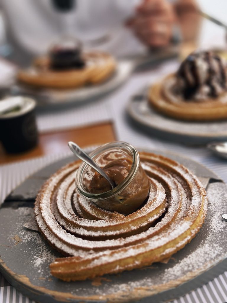 Spiral churro dusted with powdered sugar and served with a jar of caramel