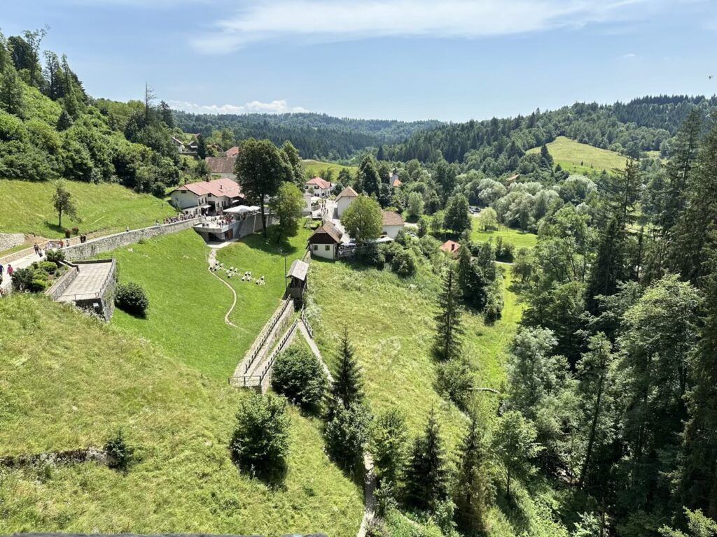 Lush green valley and village surrounding Predjama Castle under a blue sky