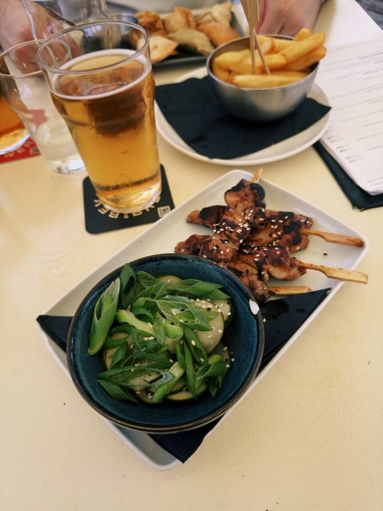 Grilled chicken skewers served with a side of cucumber salad and beer