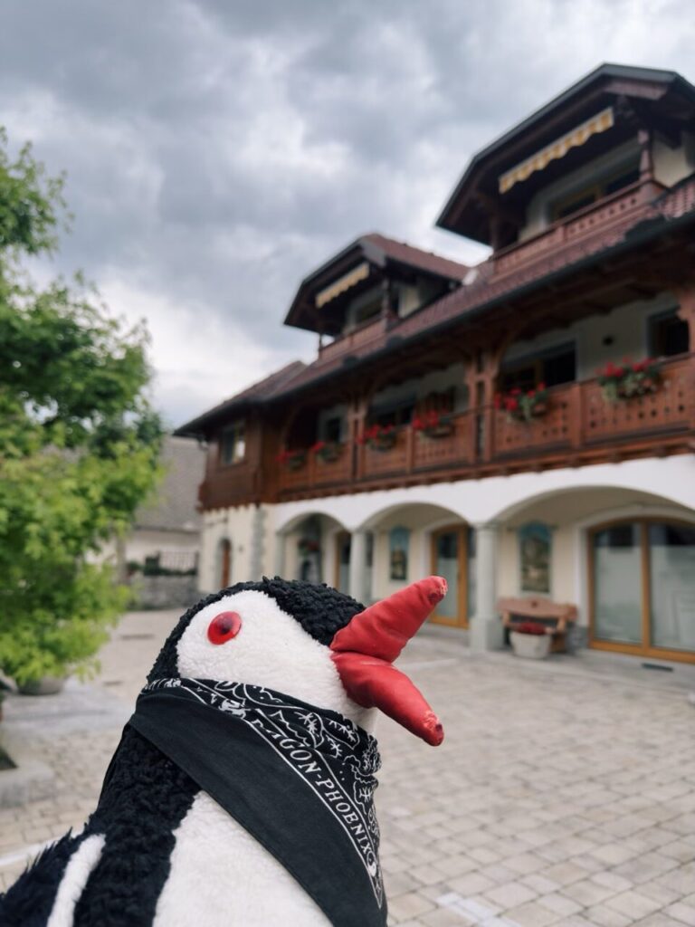 Stuffed puffin toy wearing a bandana in front of a traditional Slovenian building