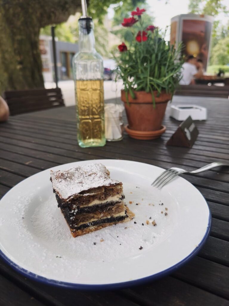 A slice of traditional Slovenian Prekmurska gibanica pastry on a plate at an outdoor restaurant