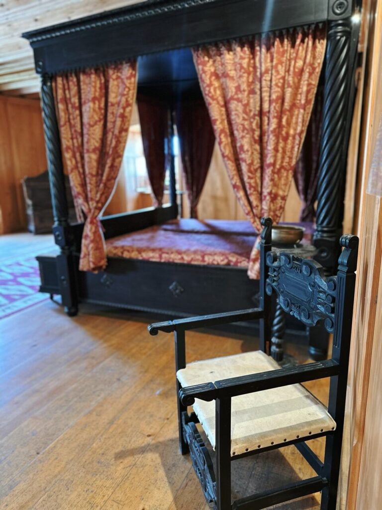 Ornate wooden chair in front of a four-poster bed inside Predjama Castle