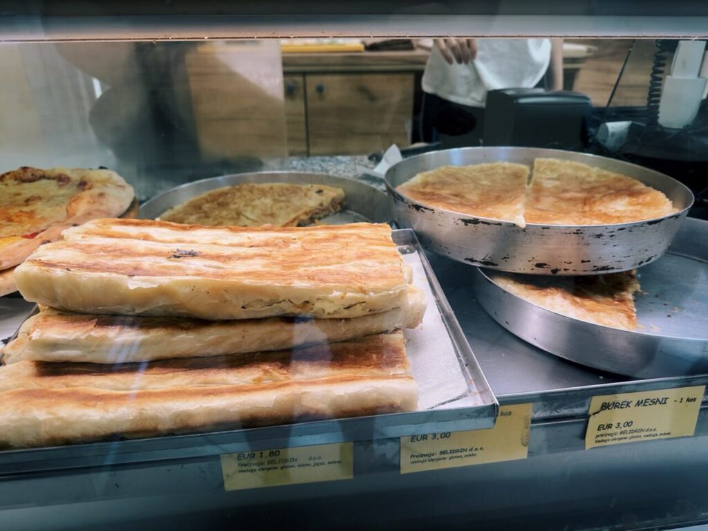 Trays of golden brown burek pastries displayed behind a glass counter in Slovenia