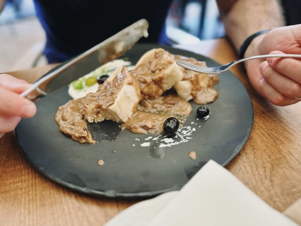 Person cutting a piece of meat covered in brown sauce on a plate