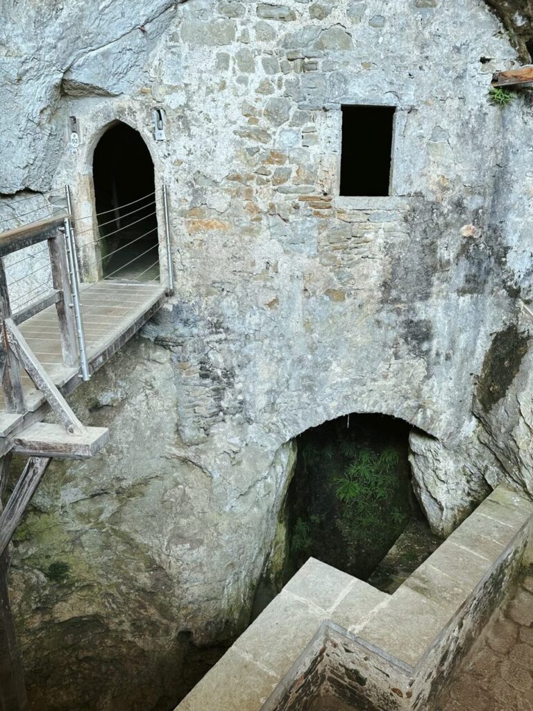 A wooden bridge leads to a stone entrance at Predjama Castle