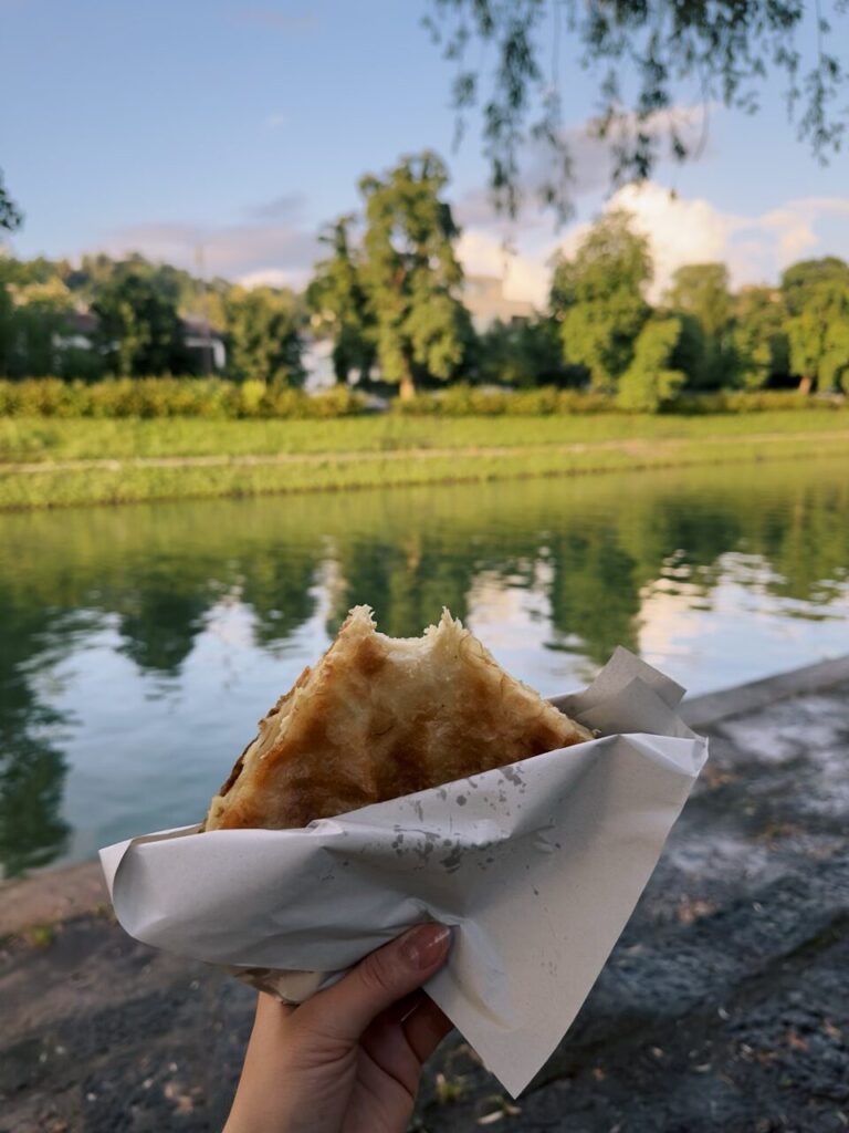 Hand holding a piece of flaky pastry by a river in Slovenia