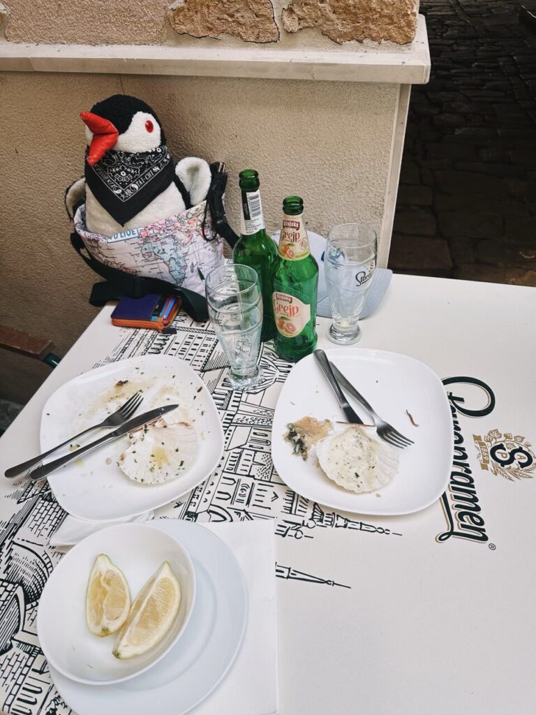 Plush penguin sits at a table with empty scallop shells and beer bottles