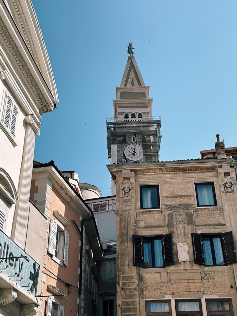 Tall bell tower rising above historic buildings in Piran under a clear sky