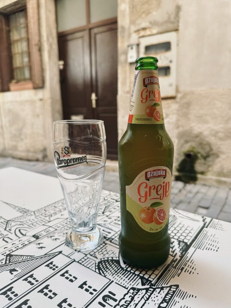 A bottle of grapefruit beer and an empty glass on a patterned table