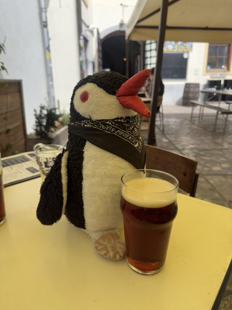 A stuffed penguin wearing a bandana sits next to a glass of beer