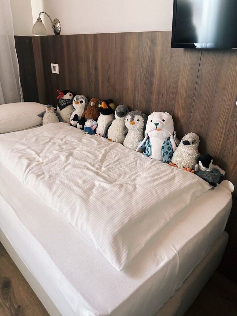 A row of stuffed penguin toys sits on a white hotel bed