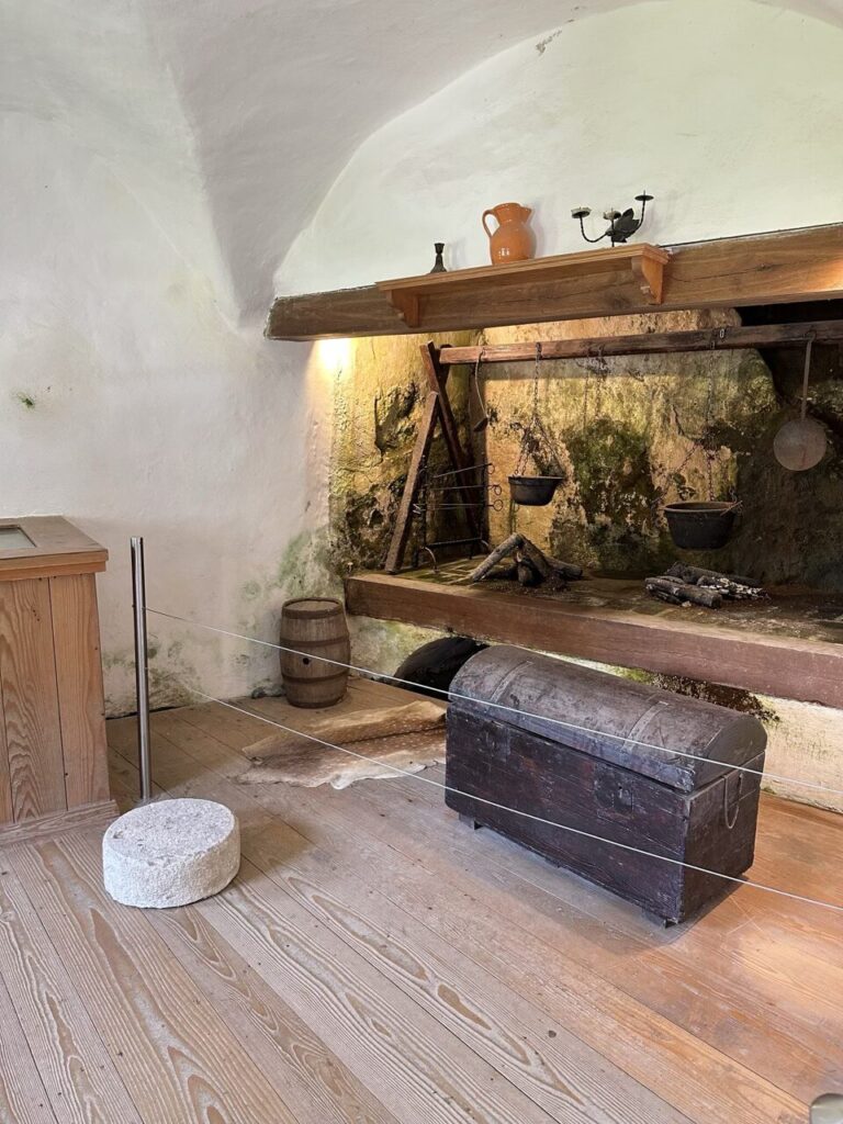 Rustic kitchen interior inside Predjama Castle featuring a stone hearth and wooden chest