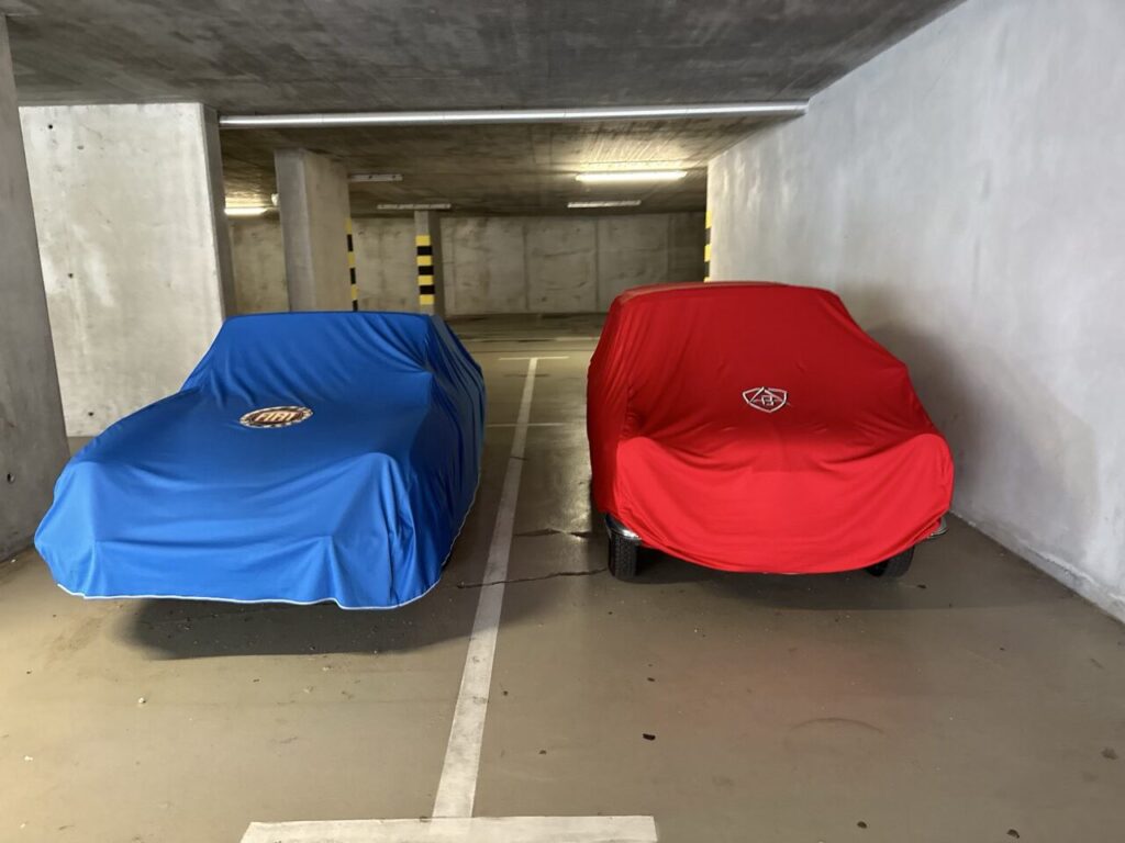 Two cars covered in blue and red fabric parked in a garage
