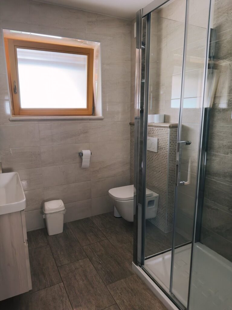 Modern bathroom with a glass shower, toilet, and window in Slovenia