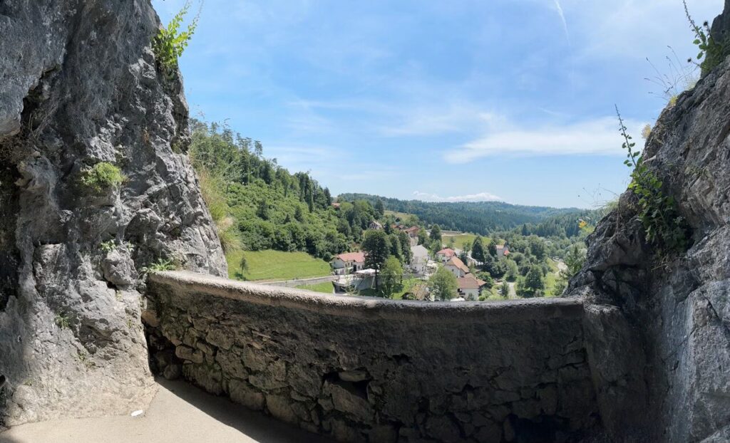 View of a valley and village from a stone balcony at Predjama Castle