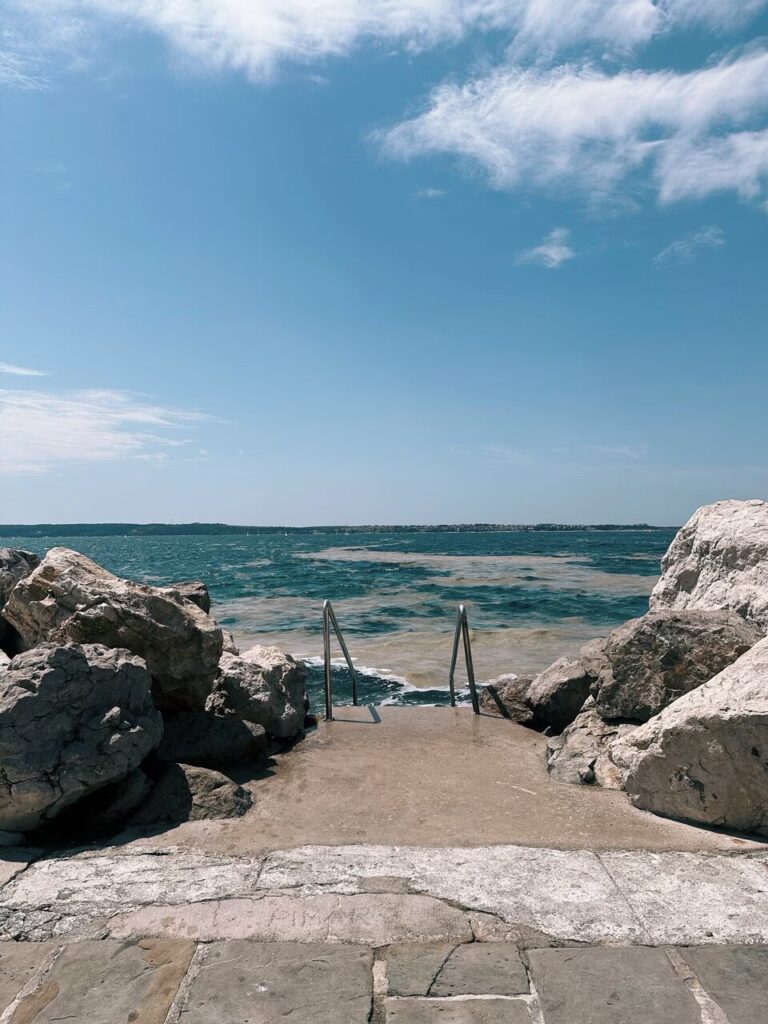 Metal ladder leading into the Adriatic Sea from a rocky Piran coastline
