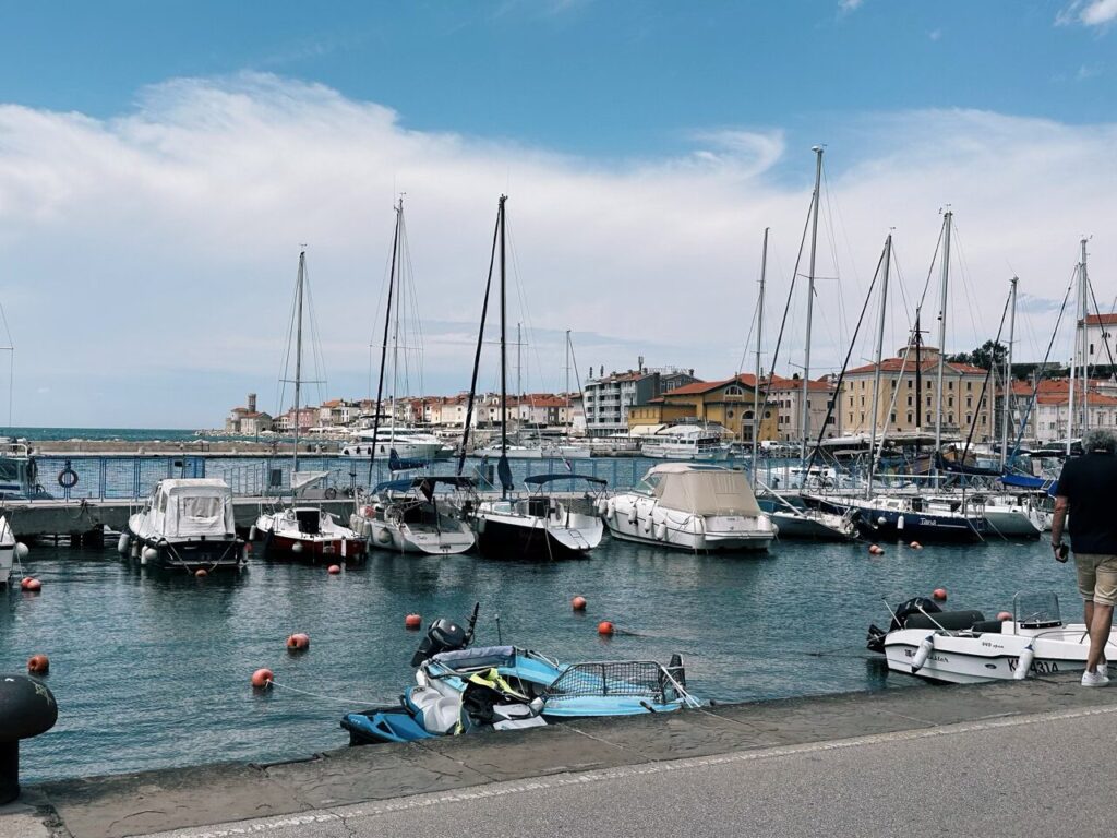 Boats docked in the harbor of Piran with buildings along the coastline