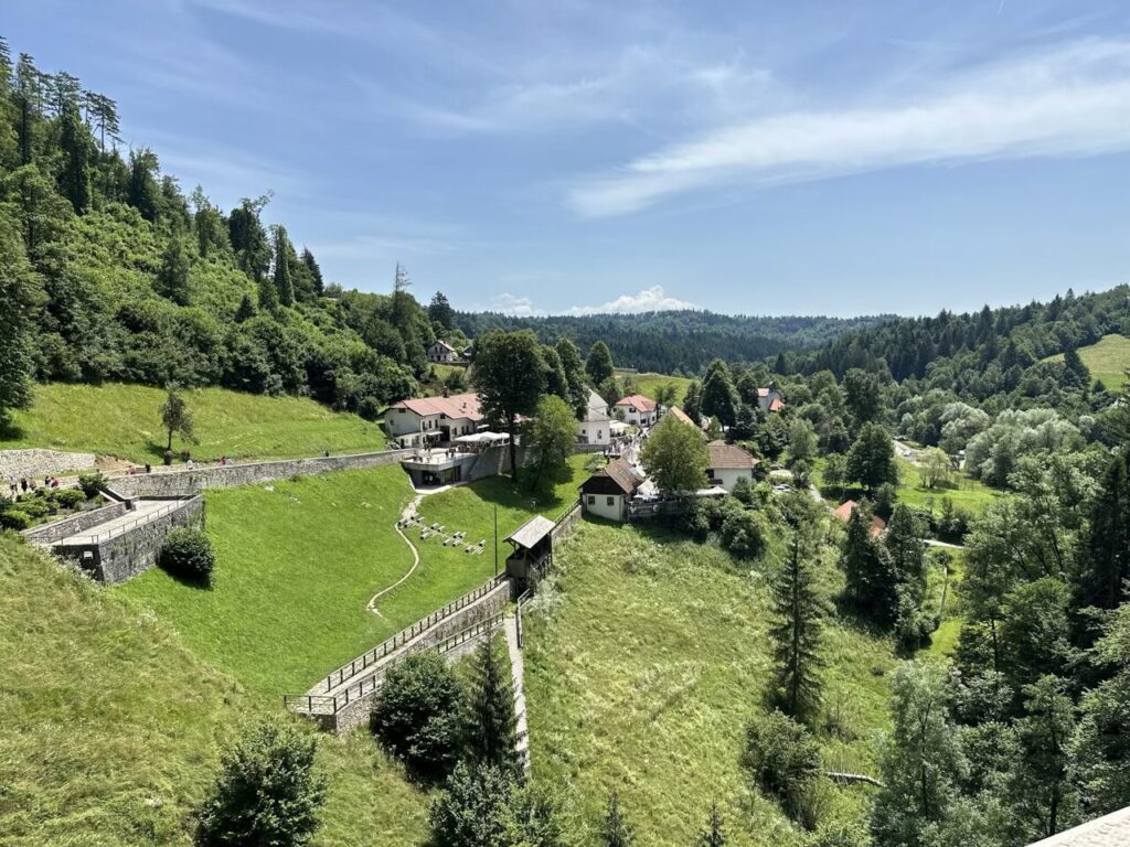 Buildings and stone walls sit nestled in a lush green valley near Predjama Castle