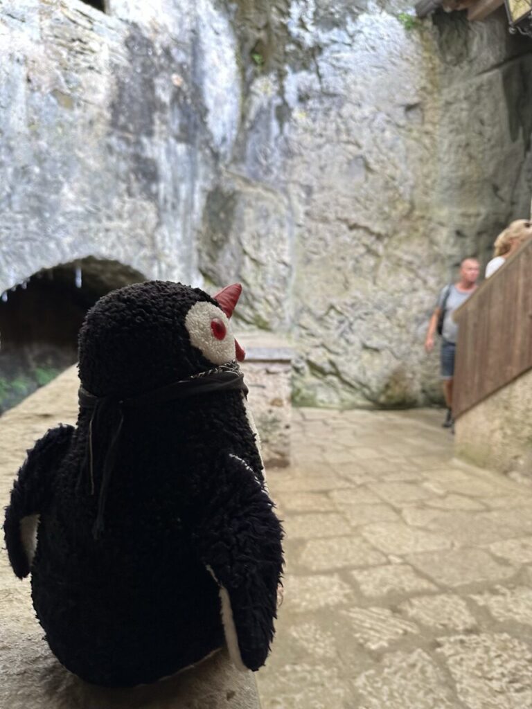 A plush penguin toy sits on a stone ledge at Predjama Castle