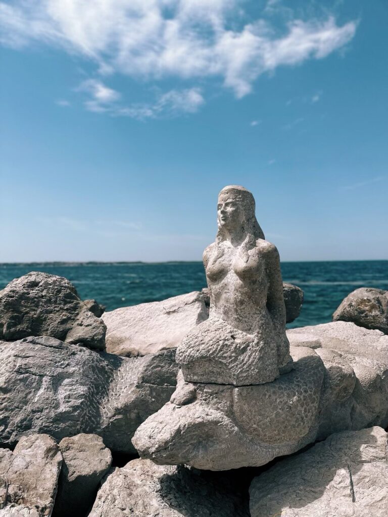 Stone mermaid statue perched on rocks overlooking the sea in Piran